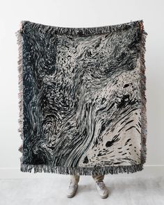 a black and white blanket with fringes on it in front of a white wall