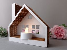 a small white house with a candle in the center and flowers around it on a table