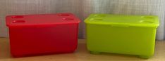 two plastic containers sitting next to each other on top of a wooden floor near a curtain