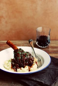 a white plate topped with meat and mashed potatoes next to a glass of wine