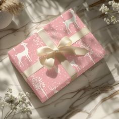 a pink gift box wrapped in gold ribbon with white deer and snowflakes on it