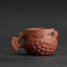 a clay fish shaped vase sitting on top of a black surface with its mouth open