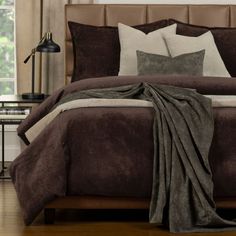 a bed with brown and white comforters in a bedroom next to a lamp on a table