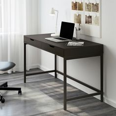 a computer desk with a laptop on it in front of a white wall and window