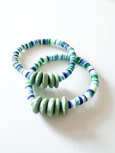 two bracelets with green, blue and white beads on a white table next to each other