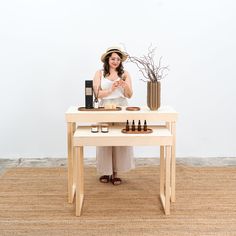 a woman standing behind a table with bottles and candles on it, in front of a white wall