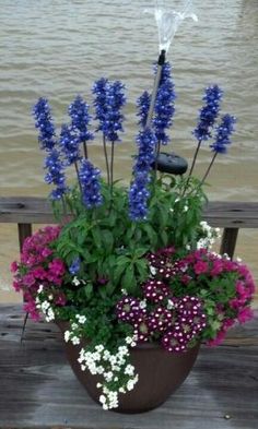 purple and white flowers in a pot on a wooden bench by the water with an umbrella