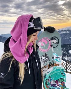 a woman holding a snowboard on top of a snow covered slope