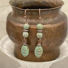 Handmade pretty sea green and copper dangle earrings. Premium Czech glass beads from the Czech Republic are used in this rustic, earthy pair of earrings. The beads are a sage - olive green with some slight bluish undertones. They have a metallic copper wash and look beautiful with antique copper accent beads, hooks, and wires. They are a nice length at 2 inches long and slender at a little over 1/4 inch wide. They come with a soft, clear, flexible rubber back to help keep your earrings securely Cheap Artisan Jewelry With Czech Glass, Earthy Green Earrings, Cheap Czech Glass Jewelry For Women, Cheap Artisan Jewelry Made Of Czech Glass, Cheap Artisan Jewelry In Czech Glass, Cheap Artisan Jewelry Made With Czech Glass, Cheap Green Czech Glass Beaded Earrings, Cheap Unique Jewelry With Czech Glass, Cheap Green Czech Glass Jewelry