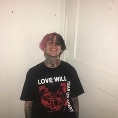 a man with pink hair and tattoos standing in front of a white wall wearing a black t - shirt