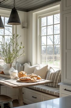 a table with bread and flowers on it in front of two large windows that look out onto a field