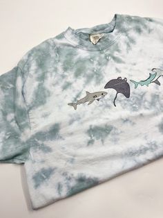 The perfect summer t-shirt for hanging out at the beach! Beautiful hand dyed sage/ocean blue tie dye that is super unique to each t-shirt! These are Comfort Colors brand and are unisex! If you have any concerns for sizing I always recommend to size up because I’d rather it be a touch big than too small! I do suggest to wash all items in cold water and dry on low heat to prevent shrinkage and fading of the tie dye. If you need your item by any particular date please email or message me before you Tie Dye Shirt Ideas, Beach Tshirt Ideas, Shark Tshirts, Shark Clothes, Ocean Outfits, Ocean Shirt, Paint Shirts, Oversized Shirts, Shark Shirt