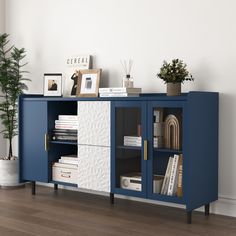 a blue and white sideboard with books on it in front of a potted plant