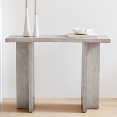 two white vases sitting on top of a wooden table next to an empty bowl