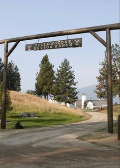 a wooden sign hanging from the side of a road next to a lush green field