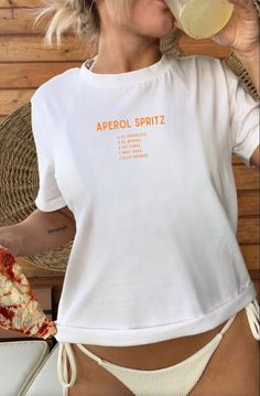 Introduce our trendy and comfortable Aperol Spritz T-Shirt! Show off your love for this delicious cocktail with this stylish shirt. Featuring a bold "Aperol Spritz" print on the front with a list of its classic ingredients. This crewneck is perfect for any casual occasion. Made from high-quality, soft and comfortable material, it's perfect for any weather. It's also a great gift for any loved one who is a fan of Aperol Spritz. Order yours today and raise a glass to good times in style! Perfect a Short Sleeve Screen Print Tops For Brunch, White Short Sleeve T-shirt For Brunch, White Crew Neck T-shirt For Brunch, Summer T-shirt With Screen Print For Brunch, Casual Screen Print T-shirt For Brunch, Graphic Print Crew Neck Tops For Brunch, Trendy Summer T-shirt For Brunch, Trendy Crew Neck Tops For Brunch, Screen Print Crew Neck T-shirt For Brunch