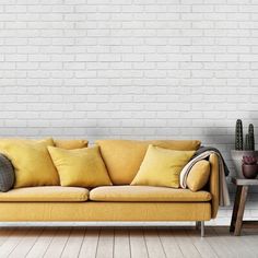 a yellow couch sitting in front of a white brick wall next to a wooden table