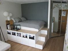 a bed sitting on top of a wooden floor next to a white dresser and stairs