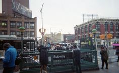 people are standing on the sidewalk near a green fence