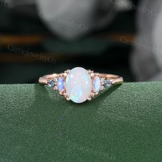 an opal and diamond ring sits on a green surface