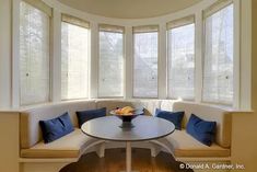 a round table with blue pillows on it in front of three windows and a white couch