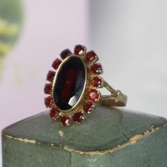 This gorgeous vintage garnet ring is centered with a halo set round cut Bohemian garnet. The centre garnet is surrounded by halo of prong set round cut garnets. The ring is crafted of 8k yellow gold and is currently a size 9 Central stone is oval shape 15x8 mm, the halo has 14 stones 3 mm each Total weight is 5.10 gram Marked inside 333 for 9 kt gold Birthstone: January. Those born in January are lucky to have the beautiful and diverse garnet as their birthstone. Garnets are commonly red but als Garnet Gold Ring, Garnet Ring Vintage, Garnet And Gold, Halo Setting, Bohemian Rings, Garnet Ring, Garnet Rings, Cluster Ring, Sell Items