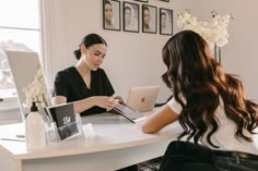 two women sitting at a table working on their laptops and talking to each other