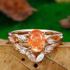 a close up of a ring on top of a leafy branch with an orange stone in the center