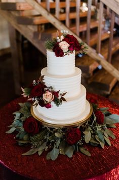 a white wedding cake with red flowers and greenery