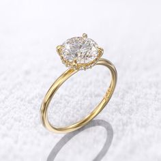 a yellow gold engagement ring with a round diamond in the center on a white background