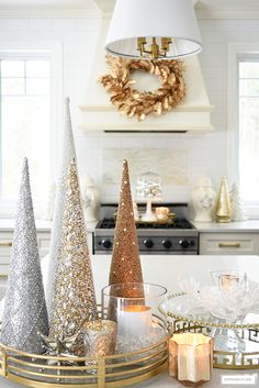 three christmas trees sitting on top of a kitchen counter next to candles and other decorations