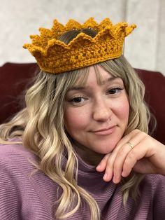 a woman wearing a crocheted crown sits on a couch and looks at the camera