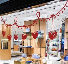 the inside of a clothing store with red hearts hanging from it's glass windows