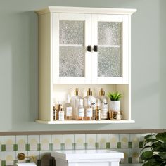 a bathroom with green and white tiles on the walls, cabinets above the toilet paper dispenser