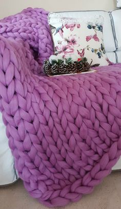 a large chunky blanket sitting on top of a white couch next to a pillow