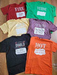 four different colored shirts with words on them sitting on a wooden floor next to each other