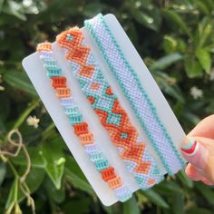 a hand holding three bracelets in front of some plants