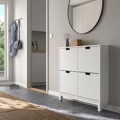 a white cabinet with drawers and a round mirror on the wall in front of it