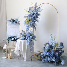 blue flowers and greenery are arranged on the floor next to a white table cloth