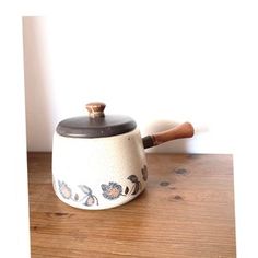 a white tea pot with a wooden handle on a wood table next to a wall