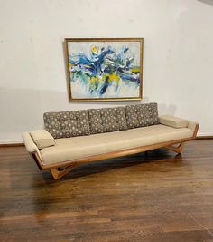 a couch sitting on top of a hard wood floor next to a framed art piece