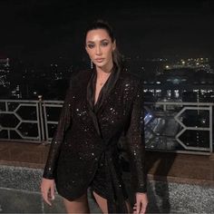 a woman standing on top of a roof next to a city at night with lights in the background