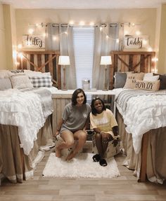 two women sitting on the floor in front of twin beds with lights strung above them