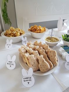 a table topped with plates filled with sandwiches and dips next to bowls of chips