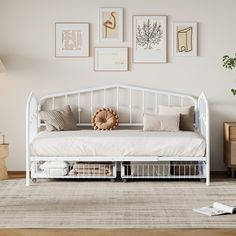 a white daybed sitting on top of a wooden floor next to a wall filled with pictures