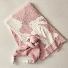 a pink towel with white rabbits on it and a stuffed animal in the corner next to it