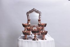 an ornately decorated mirror and three vases on a white table with a silver background