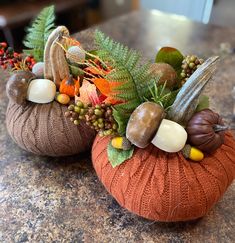 two knitted pumpkins decorated with fall foliage and acorns sit on a granite countertop