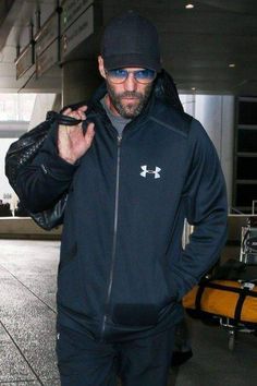 a man wearing sunglasses and a black jacket is walking through an airport with his hand in his pocket