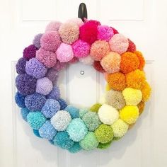 a rainbow colored wreath with pom - poms hanging on the front door,